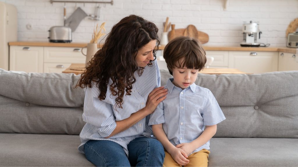 Contextual safeguarding, female adult comforts sad looking young boy on a grey sofa.