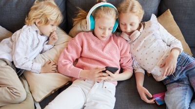 Three children gathered together on a sofa playing online. 