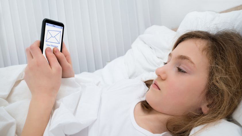 A girl looking at her mobile phone in her bed.