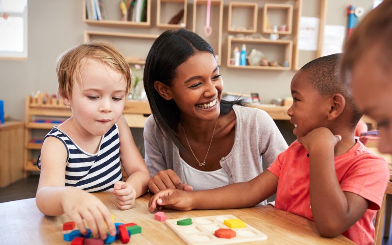 early-years-thumnail Early years practitioner playing a shape-sorting game with two young children