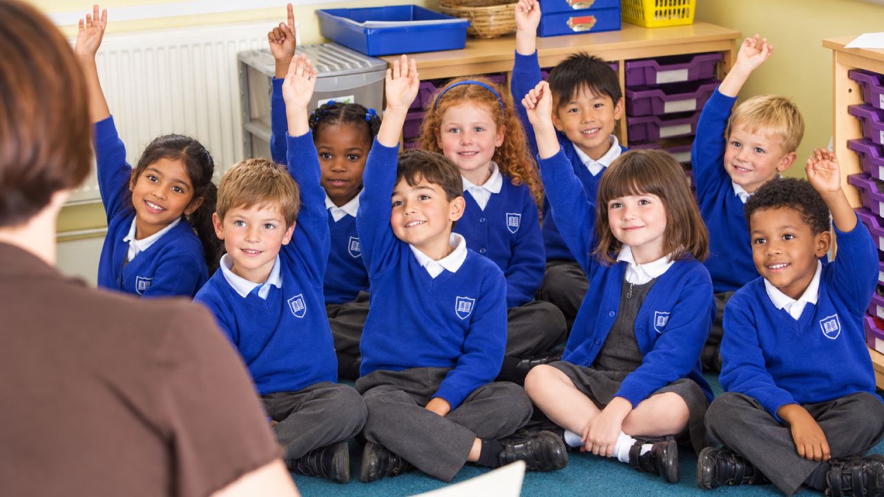education-sector-header Primary school children in uniform raising their hands in class