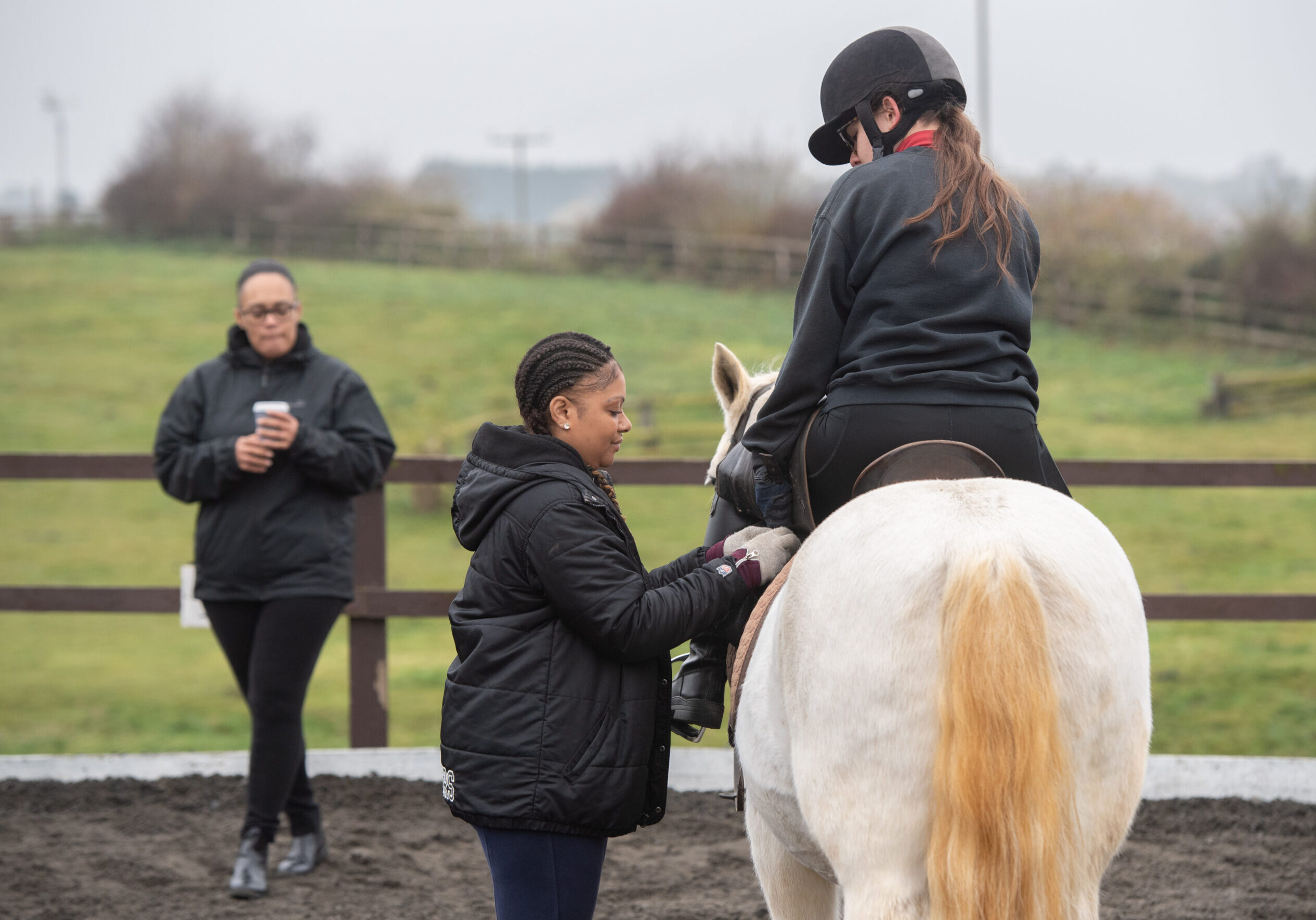 Instructor helping a young rider adjust a stirrup at an outdoor riding arena