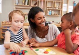 Early years practitioner playing a shape-sorting game with two young children